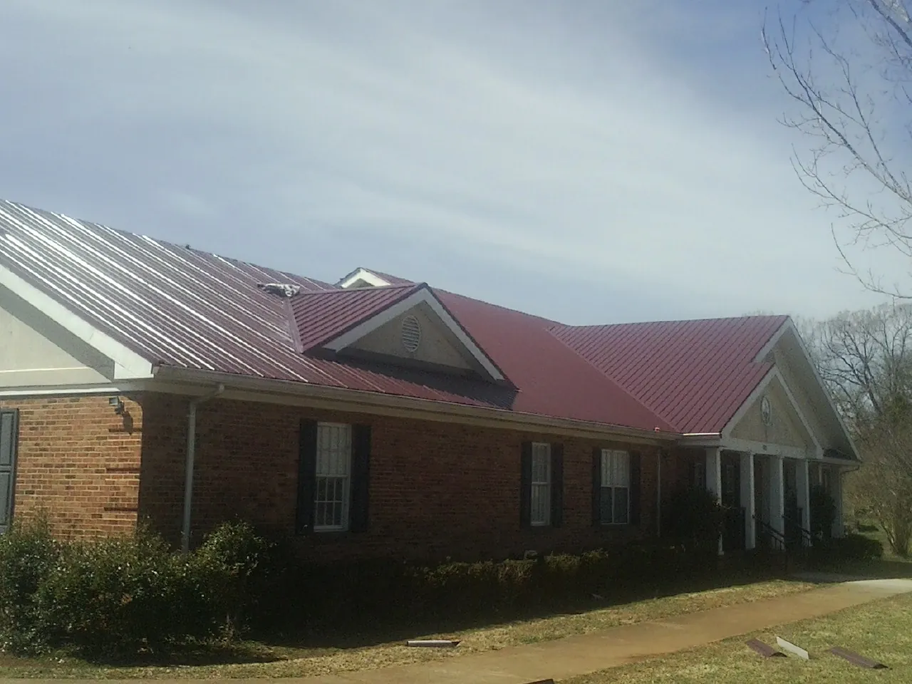 Red metal roof with gabled entries on a long brick building, from a Hail Damage Roof Repair job in Nocatee