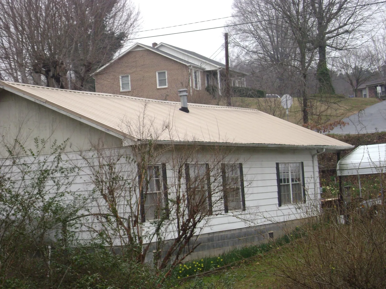 Tan metal roof on a white sided house set into a hillside — Commercial Roofing by Roofing Brothers in Nocatee
